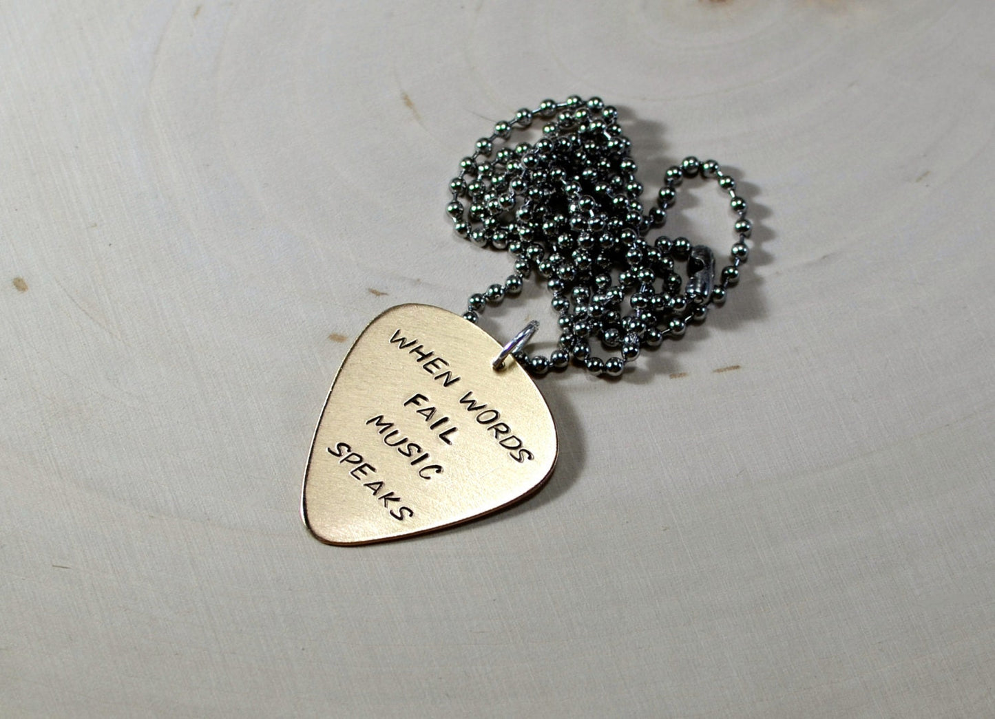 Bronze guitar pick necklace stamped with When words fail music speaks