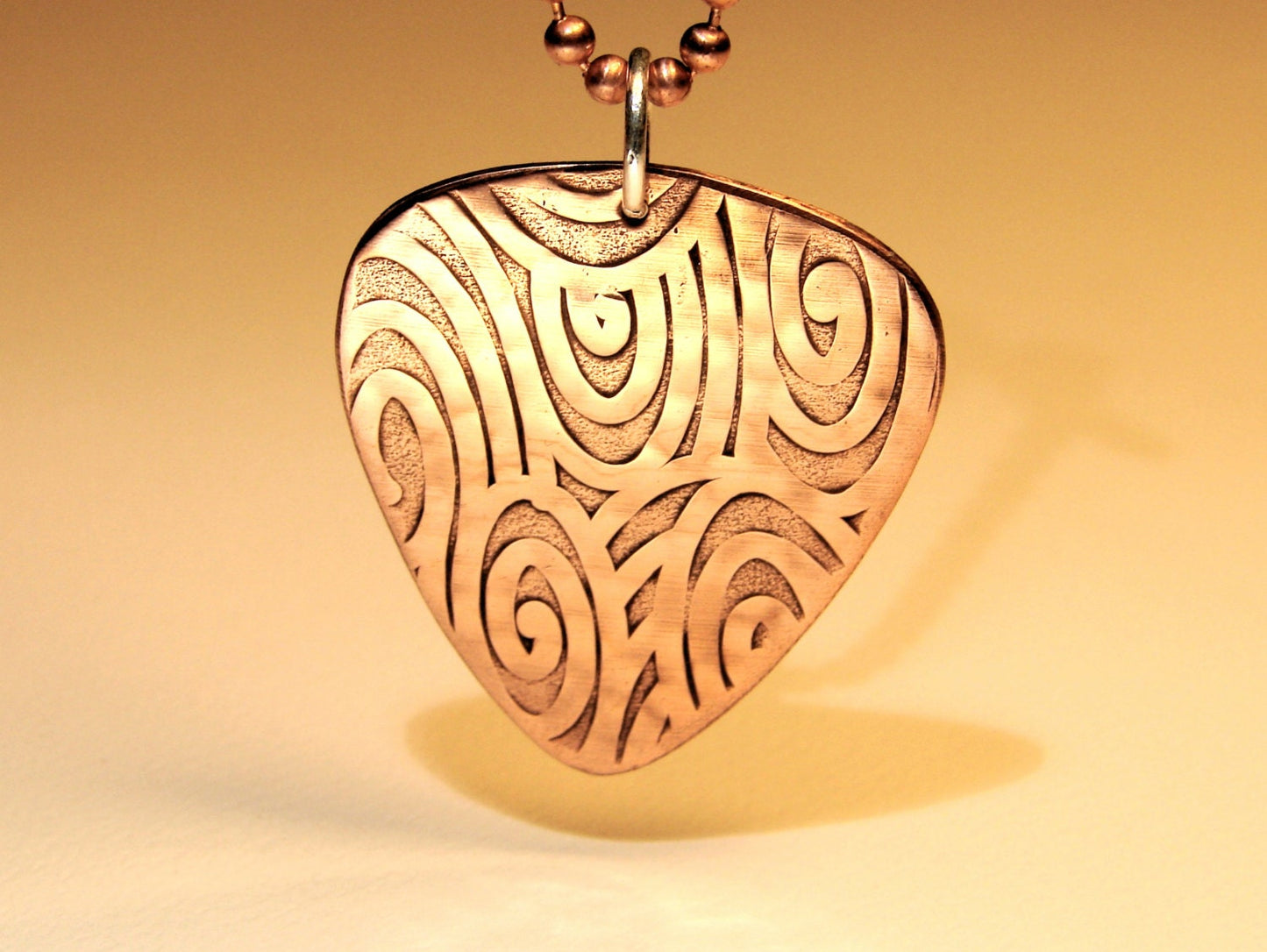 Guitar pick necklace with swirling waves in copper