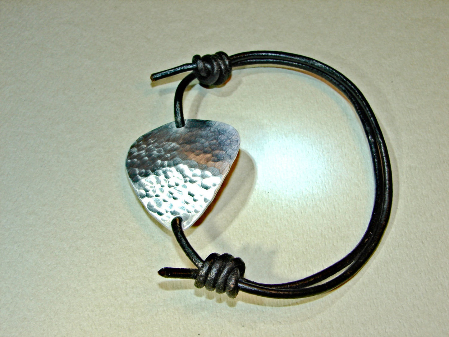 Hammered aluminum guitar pick on black leather cord