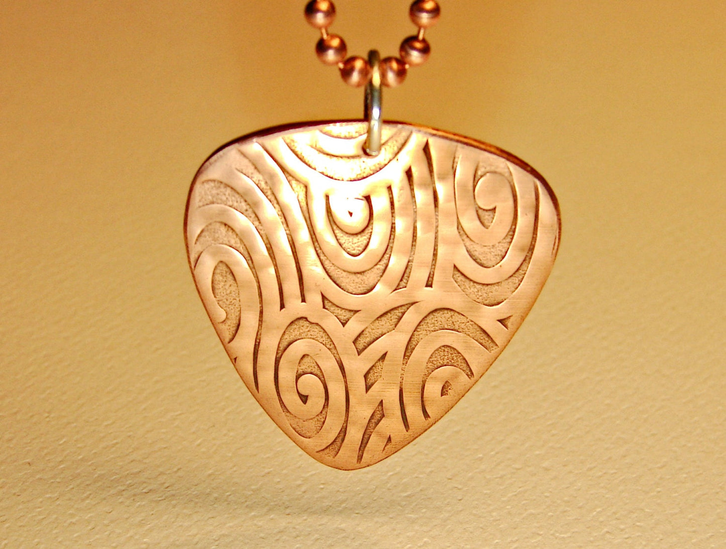 Guitar pick necklace with swirling waves in copper