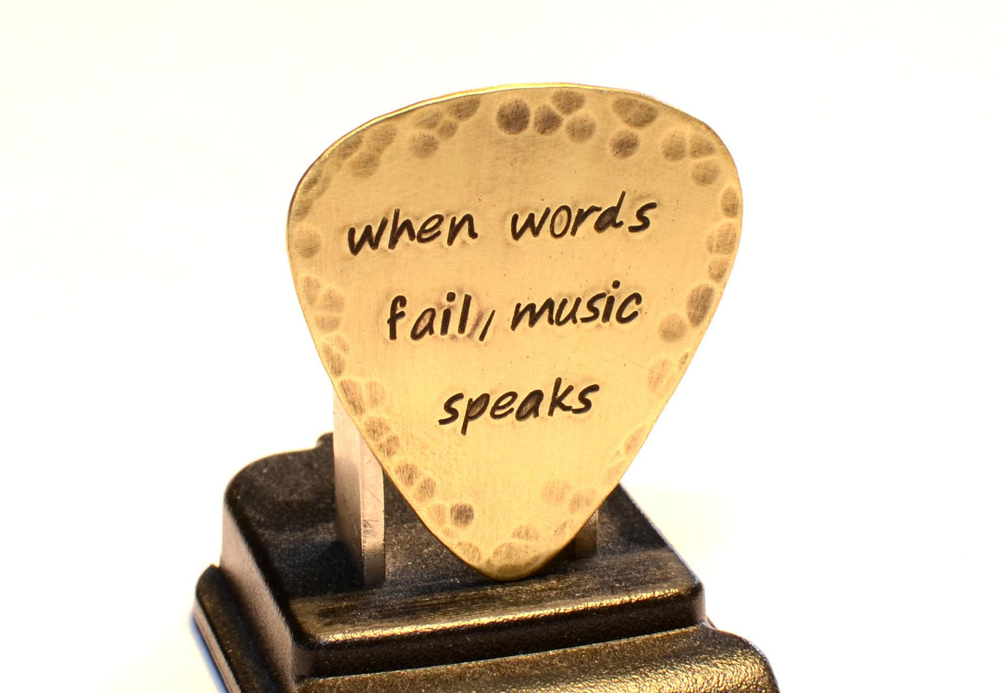 When Words Fail Music Speaks stamped on a rustic handcrafted brass guitar pick