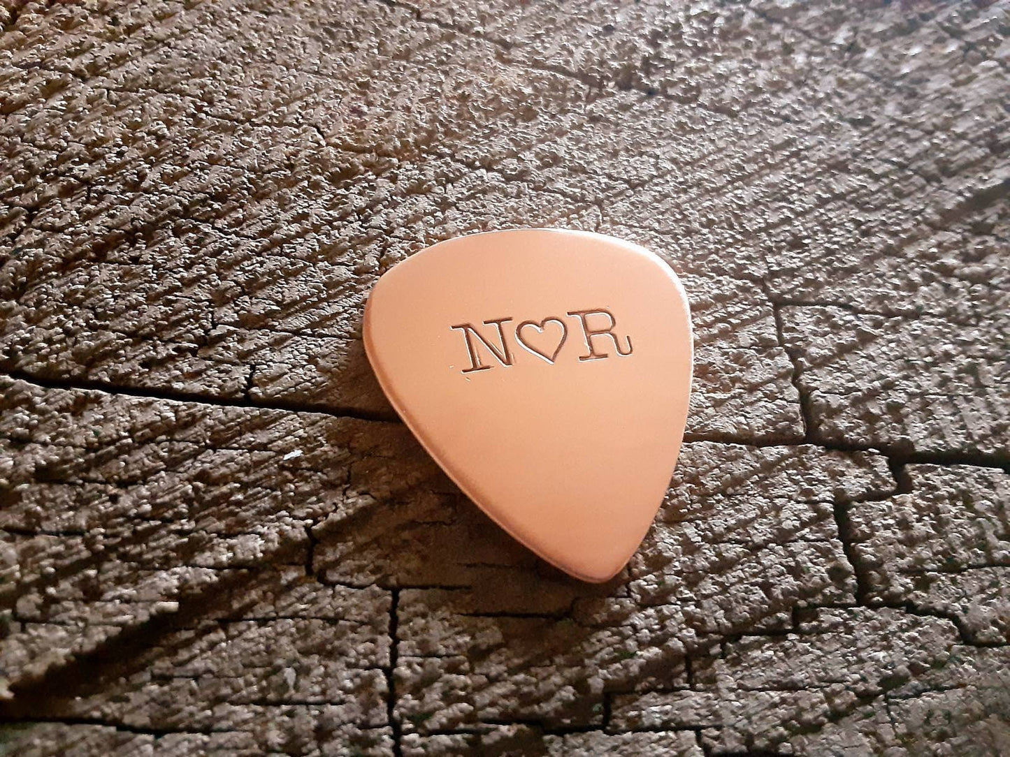 Initials and heart on a copper guitar pick