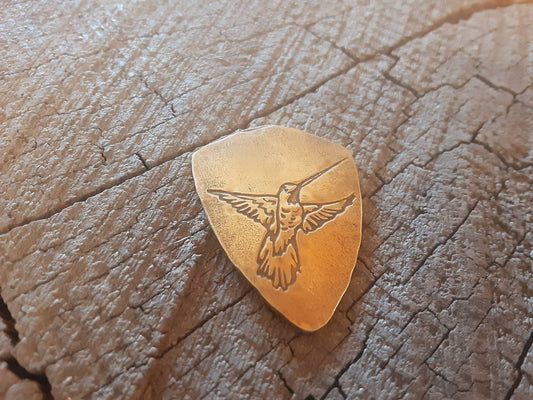 Bronze guitar pick ready for playing with a humming hummingbird