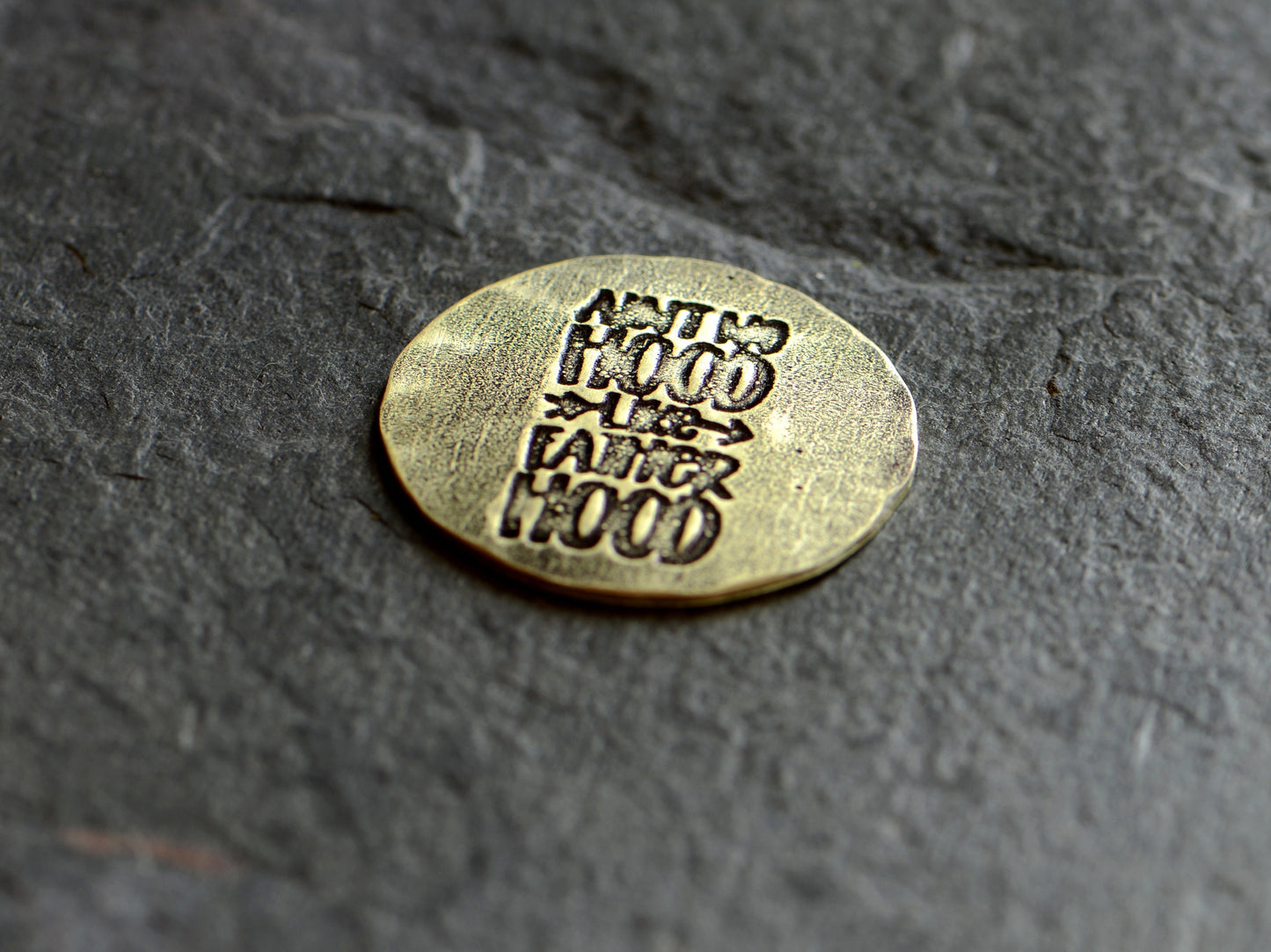 Golf ball marker stamped with " Ain't no hood like fatherhood" in brass