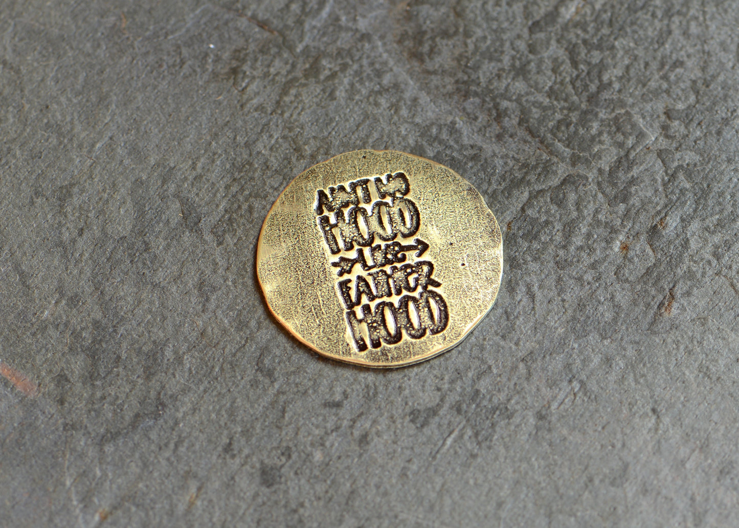 Golf ball marker stamped with " Ain't no hood like fatherhood" in brass