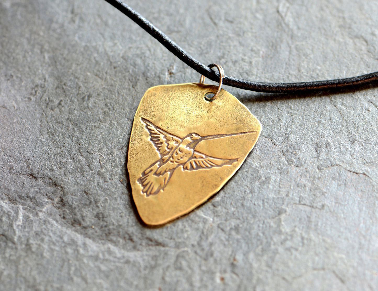 Brass shield shaped guitar pick with hummingbird and adjustable leather cord