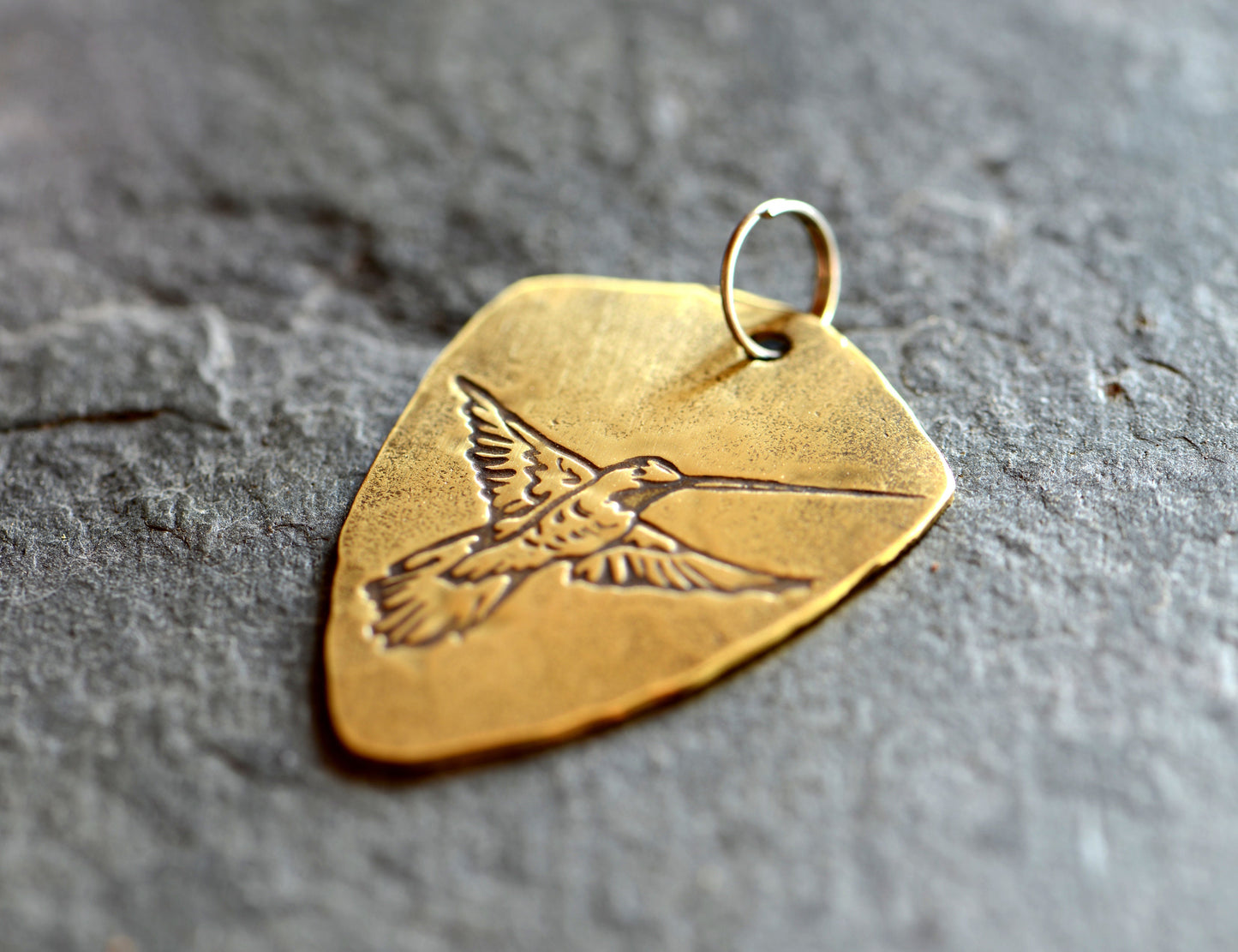 Brass shield shaped guitar pick with hummingbird and adjustable leather cord