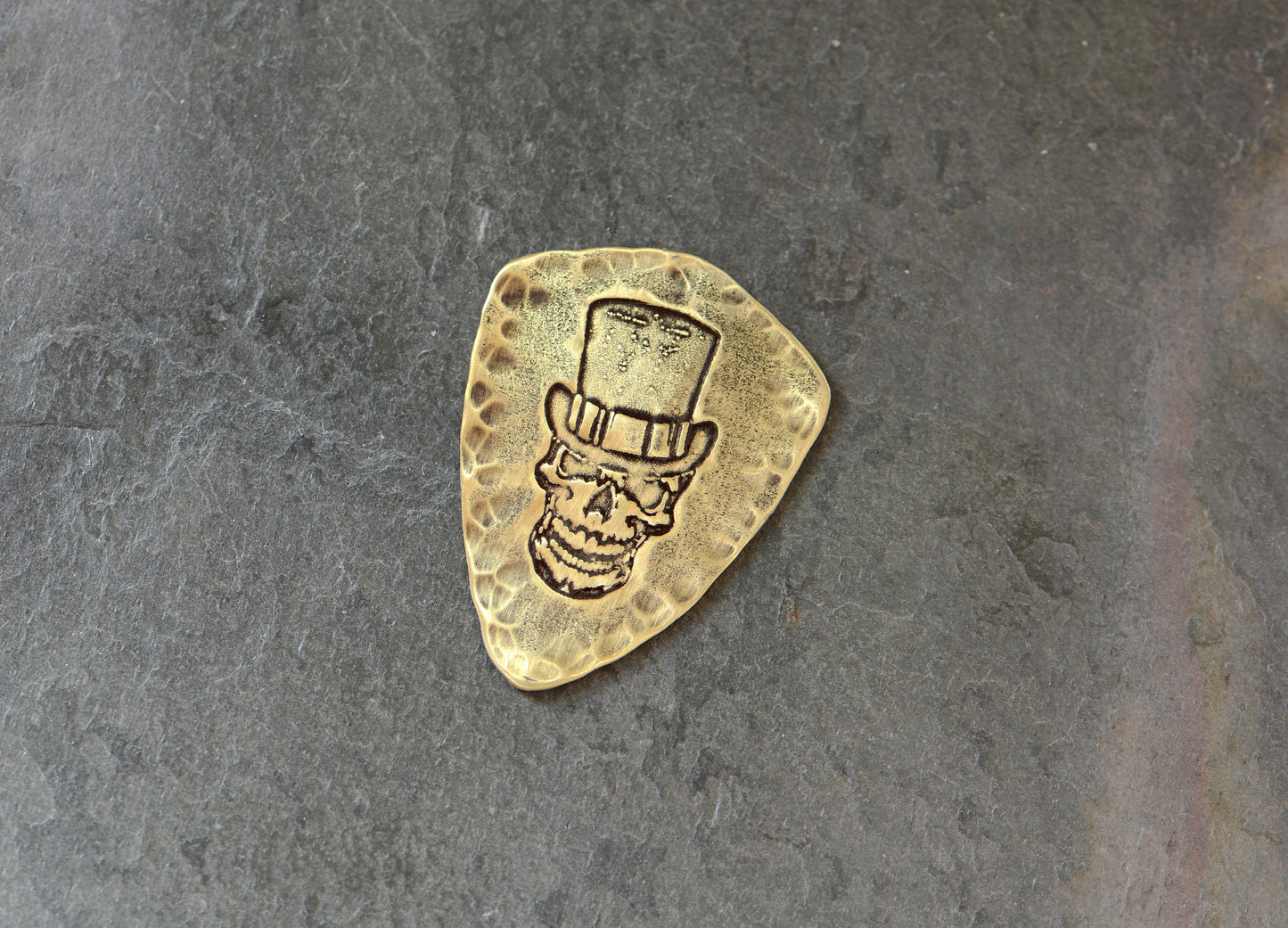 Shield shaped brass guitar pick with skull and top hat