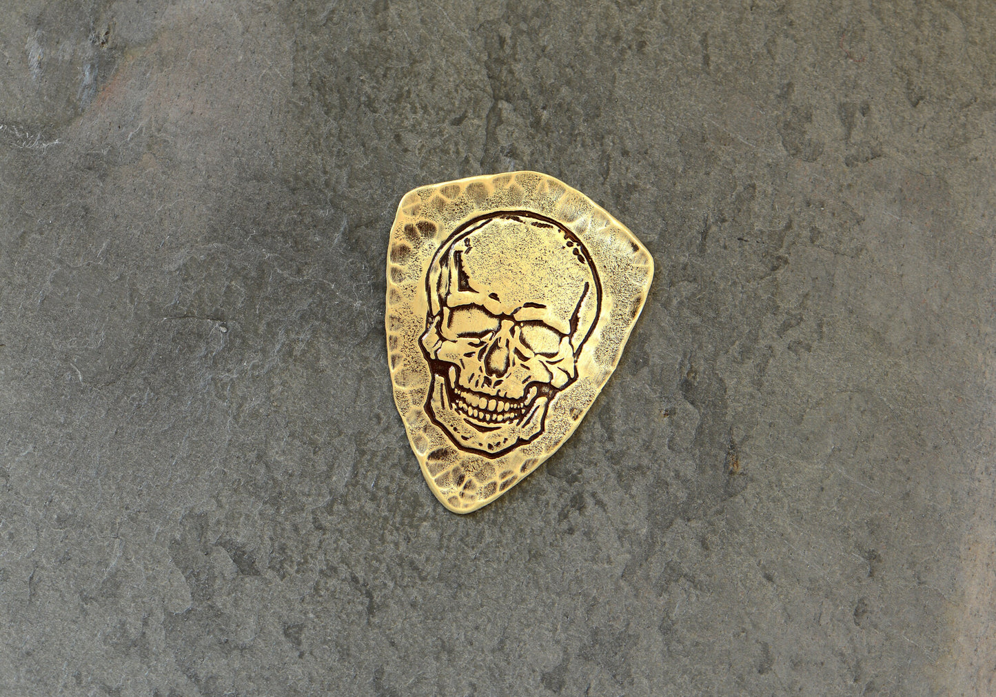 Shield style brass guitar pick with skull design