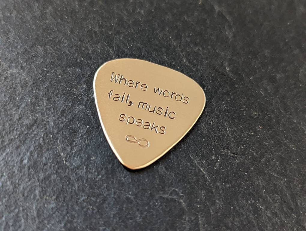 Playable bronze guitar pick stamped with when words fail, music speaks and infinity sign