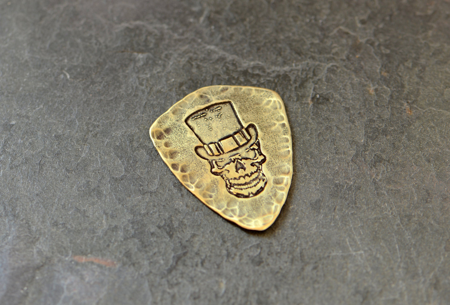 Shield shaped brass guitar pick with skull and top hat