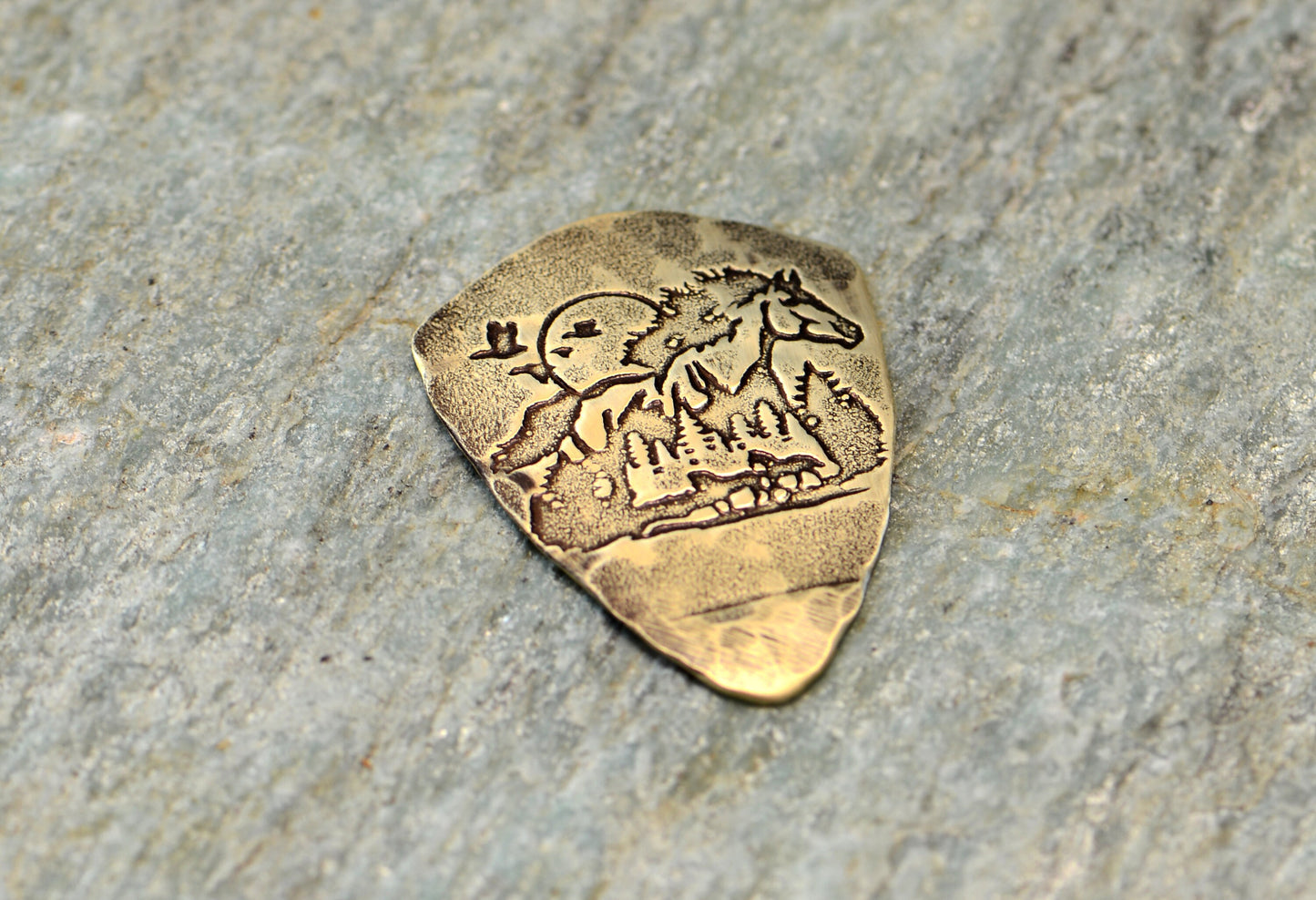 Shield shaped brass guitar pick with horse and forest