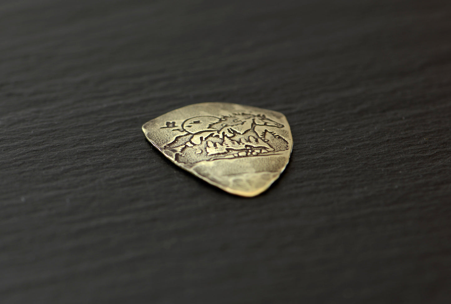 Shield shaped brass guitar pick with horse and forest
