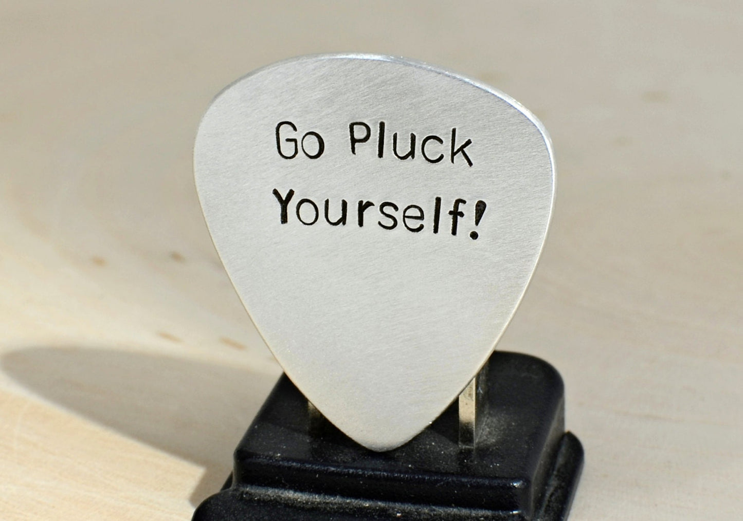 Silver guitar pick with Go Pluck Yourself