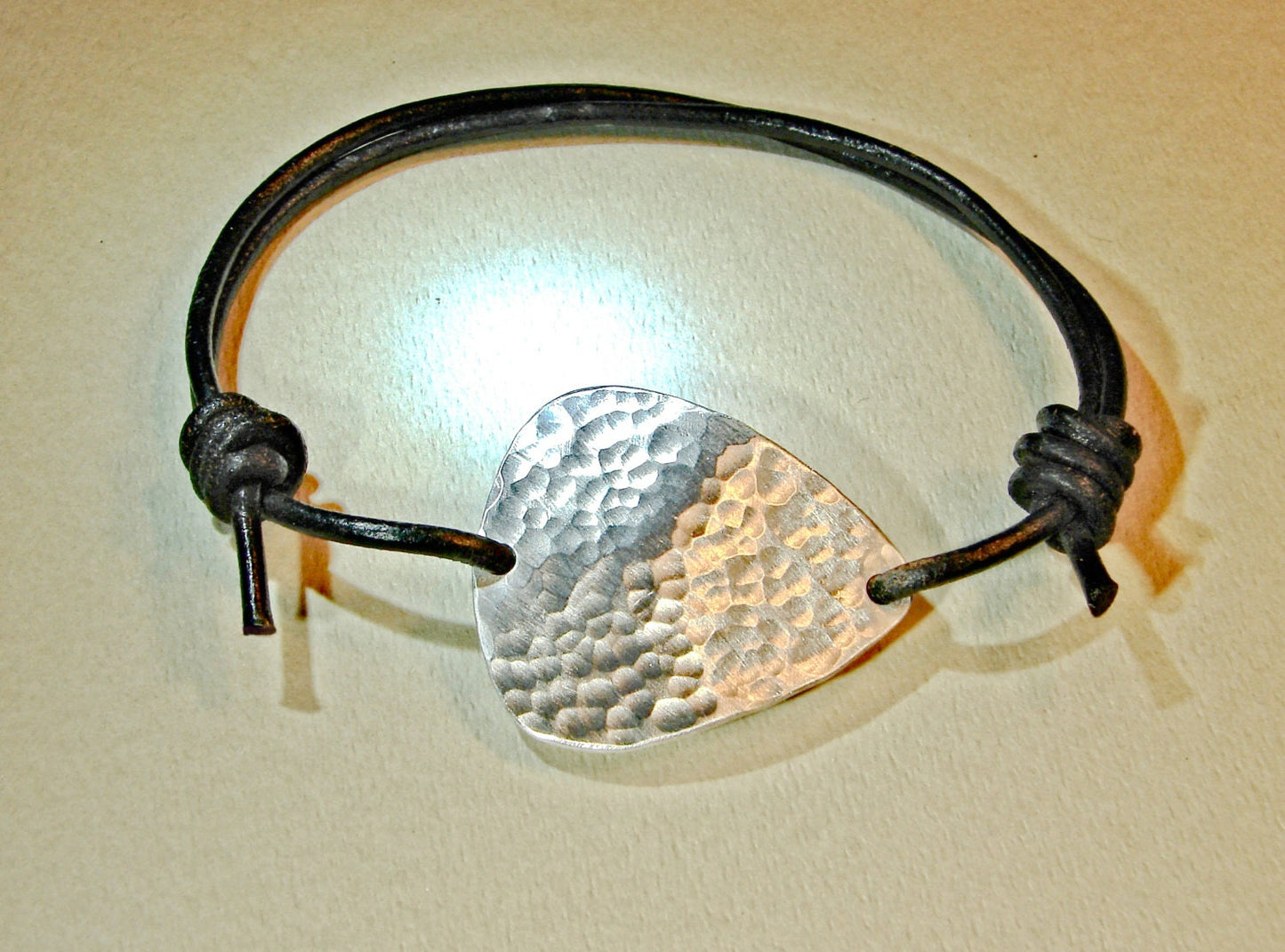 Hammered aluminum guitar pick on black leather cord