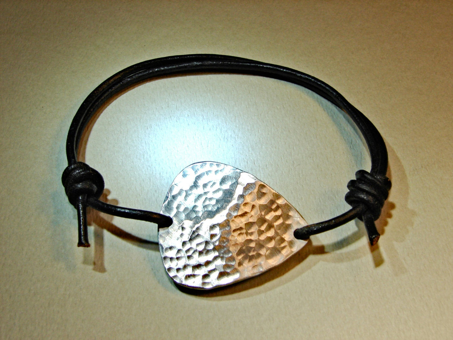 Hammered aluminum guitar pick on black leather cord